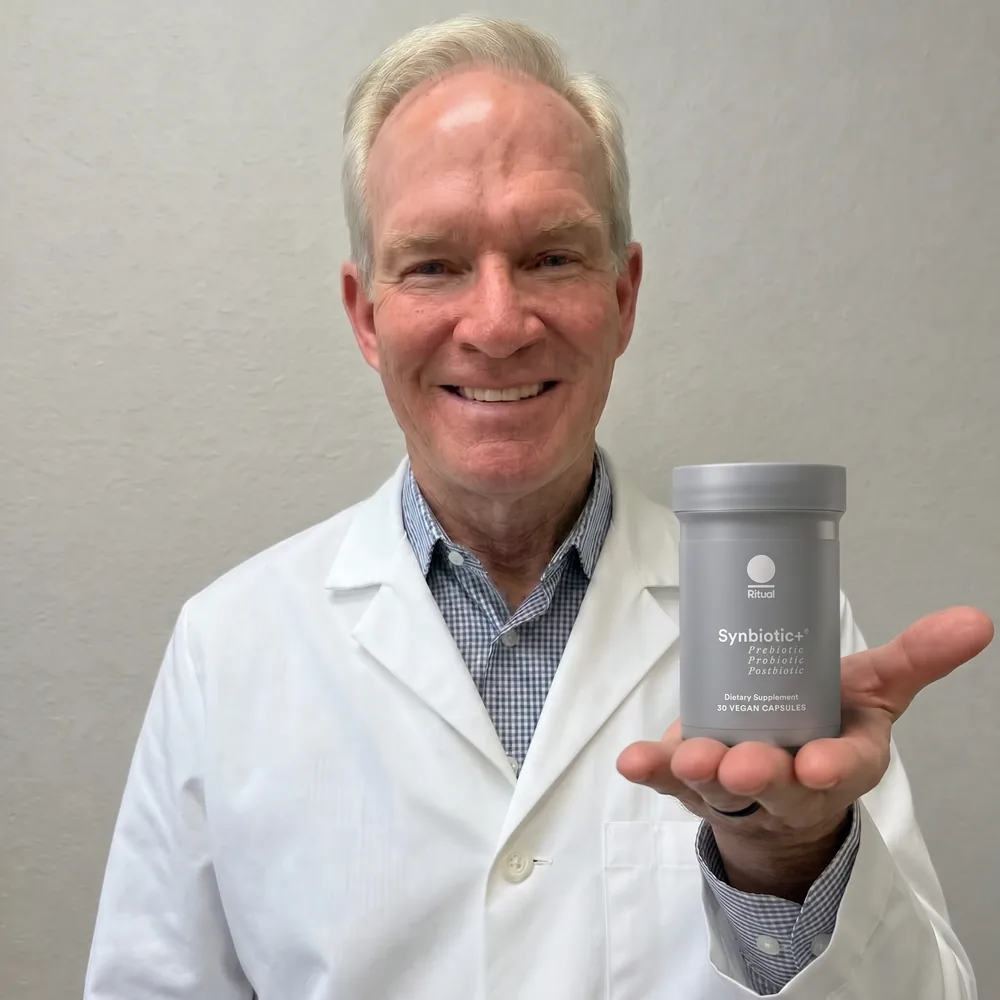A physician in a white coat smiling with the Ritual Synbiotic+ bottle resting on an open palm.